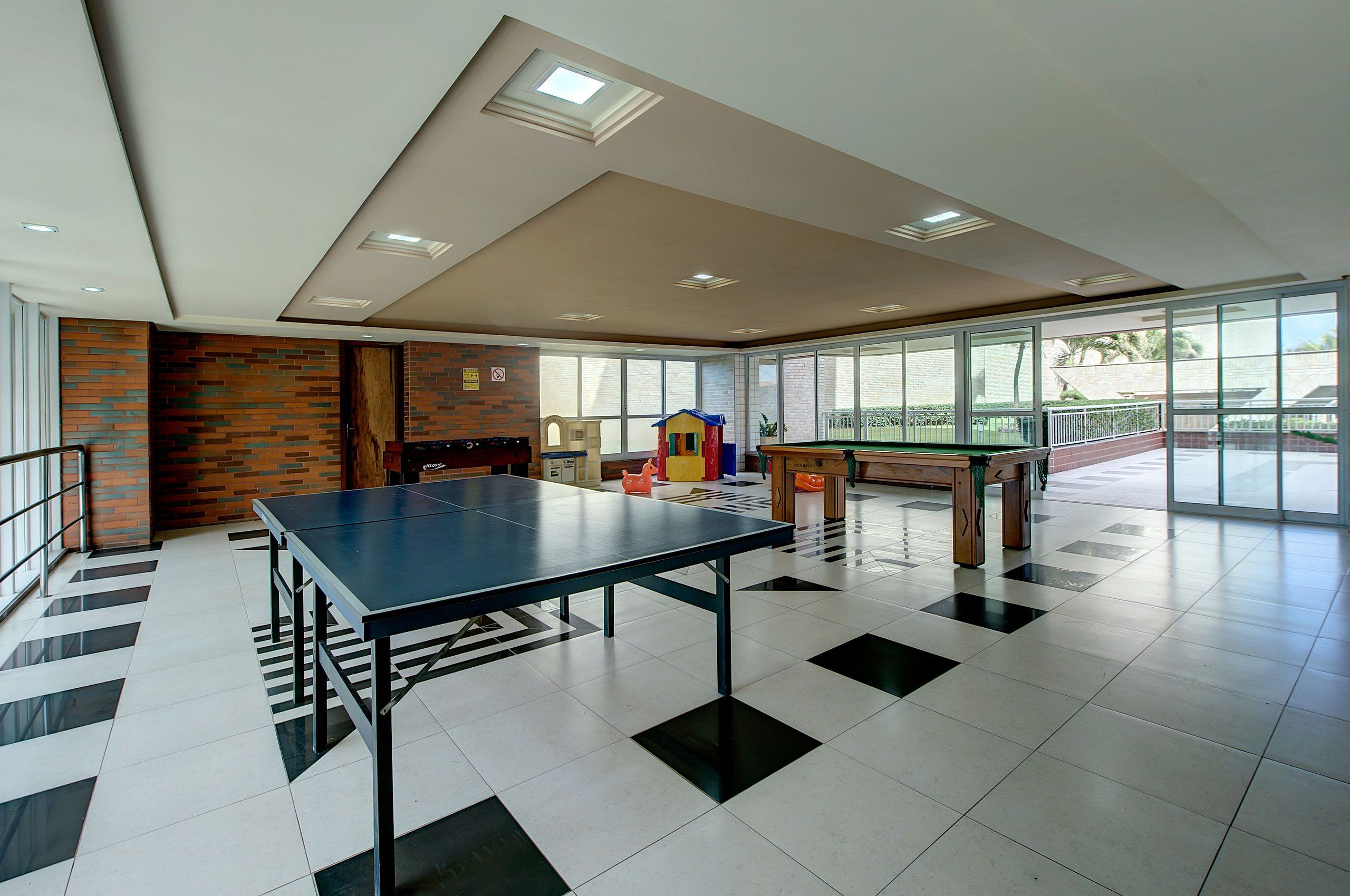 A spacious room with a ping pong table, a play area with toys, and large windows offering a view of the outdoors.