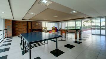 A spacious room with a ping pong table, a play area with toys, and large windows offering a view of the outdoors.