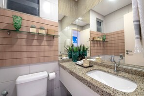 Un bagno moderno con un piano di lavoro in granito, un lavabo bianco, uno specchio e un water.