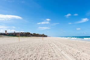 A wide sandy beach with footprints leading to the ocean, a building with a tower, and a clear blue sky. - Scopa Beach #c1-200 - Seafront by Carpediem (Aquiraz)