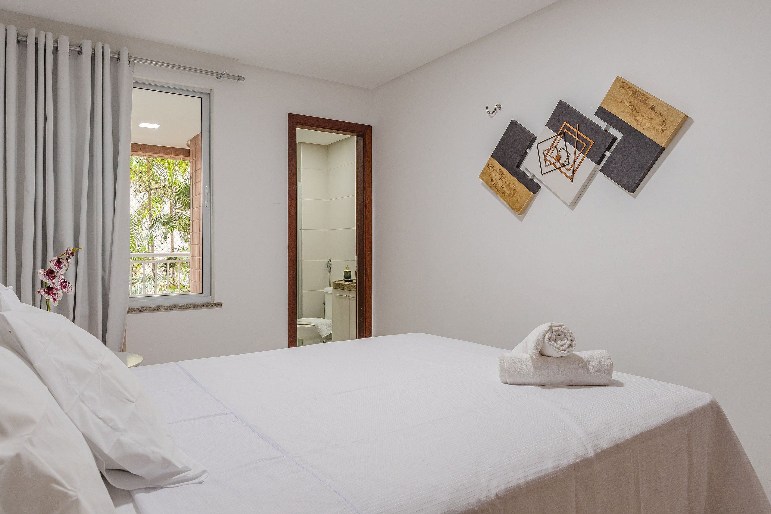 Una habitación de hotel con una cama, una ventana con cortinas, un baño visible a través de la puerta y una pared decorada con cuadros.