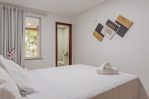 Camera d'albergo con un letto, una finestra con tende, un bagno parzialmente visibile attraverso la porta e una parete decorata con quadri.