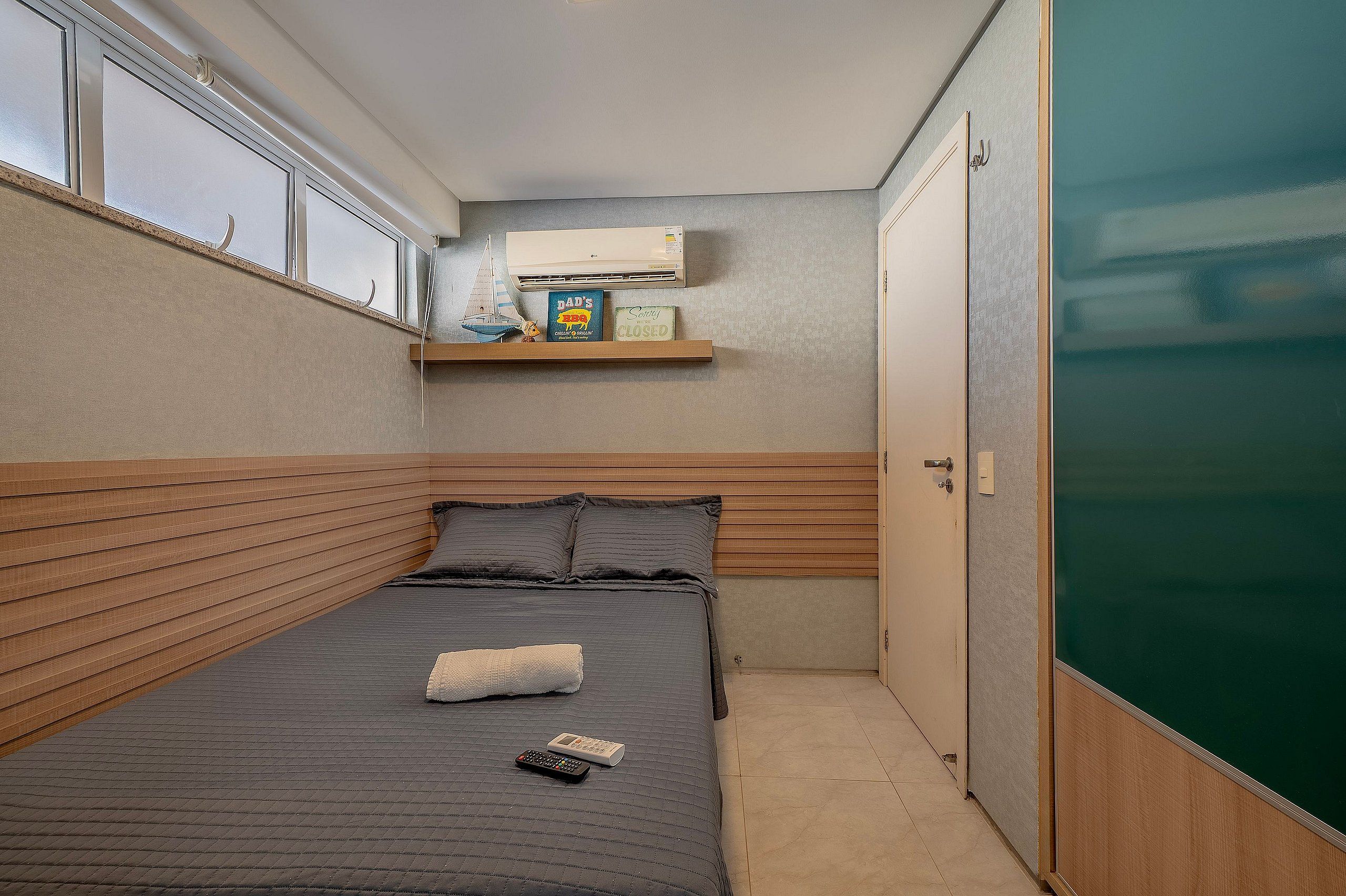 Una habitación pequeña y estrecha con una cama, un estante con objetos y una puerta.
