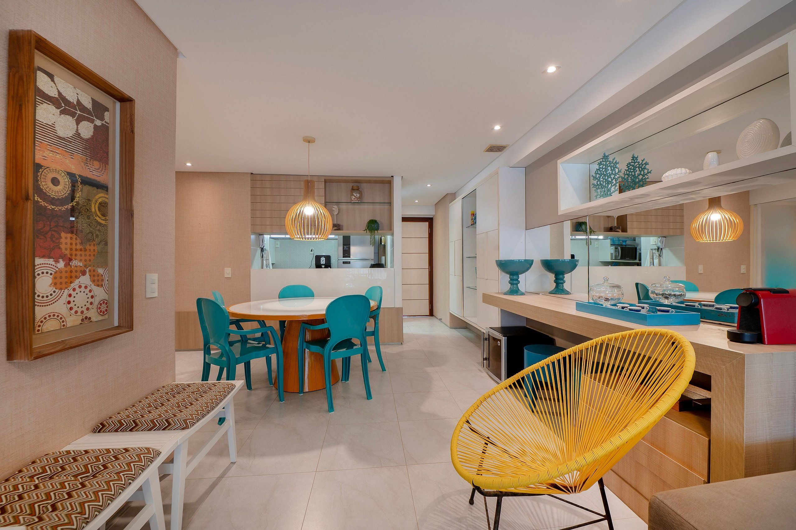 Una cucina moderna con zona pranzo, caratterizzata da un tavolo rotondo, sedie color petrolio e una sedia gialla in fibra naturale.