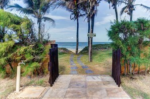 A pathway leading to a beach with palm trees and a sign indicating a beach area. - Scopa Beach #c1-200 - Seafront by Carpediem (Aquiraz)