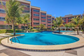 A swimming pool with a circular design, surrounded by palm trees and a multi-story building with balconies. - Scopa Beach #c1-200 - Seafront by Carpediem (Aquiraz)