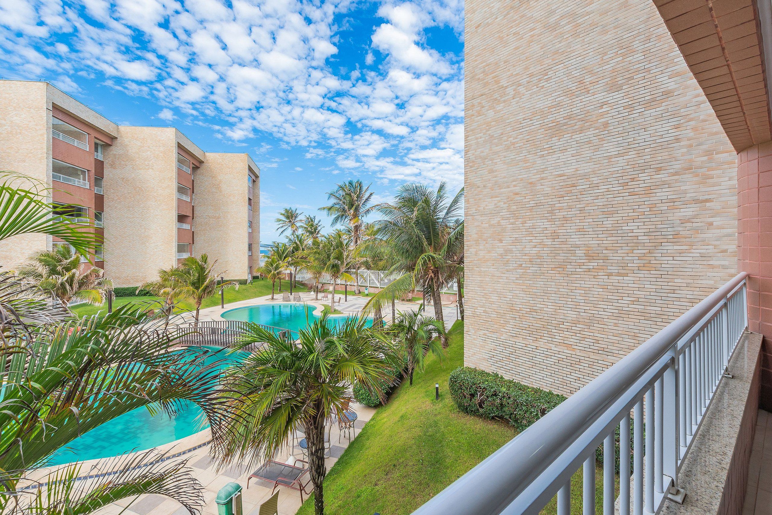 A hotel with a pool, palm trees, and a clear blue sky.