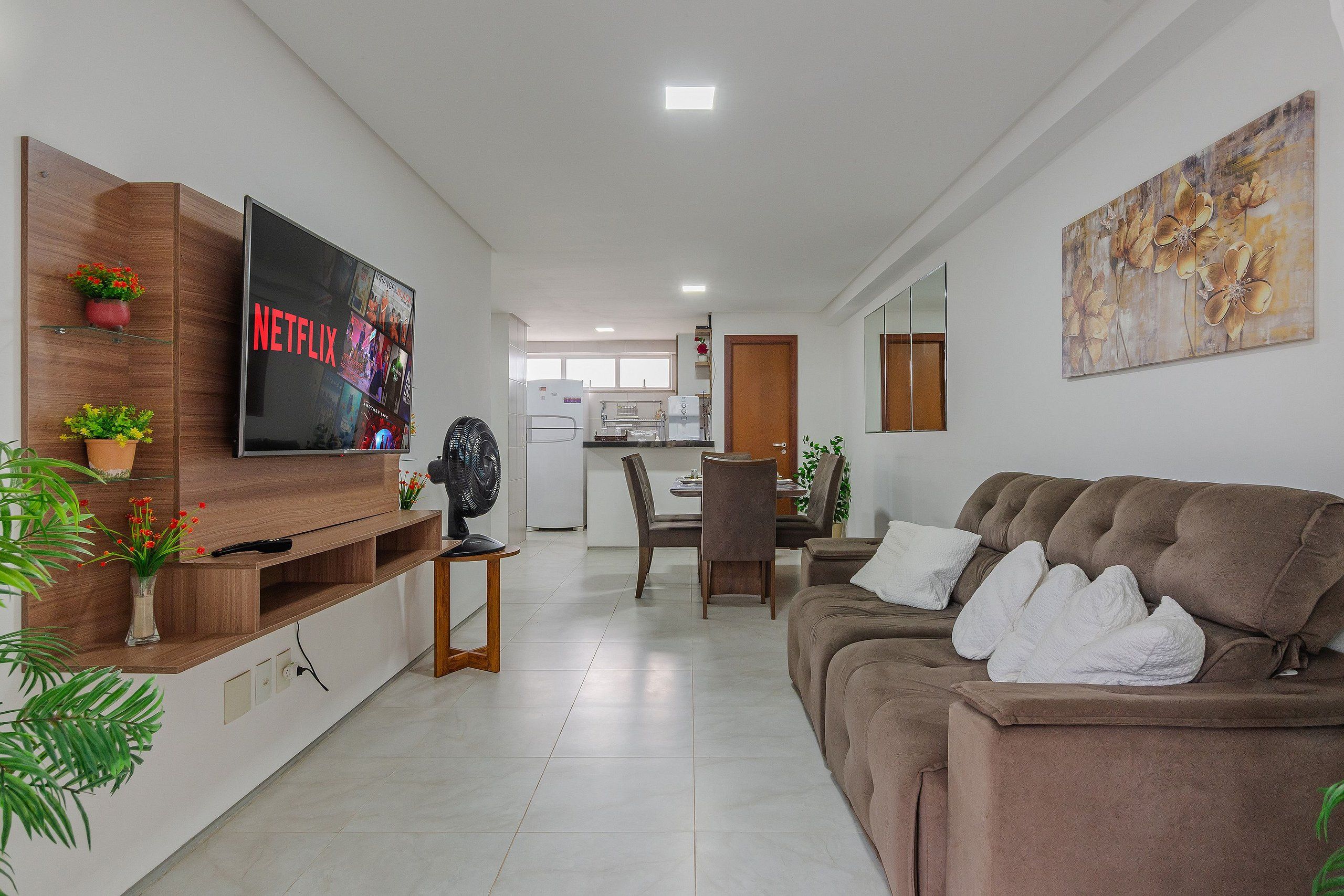 Una sala de estar moderna con televisor de pantalla plana, un sofá marrón y una zona de comedor con una mesa y sillas.