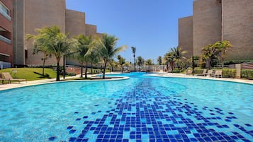 Una piscina con mosaicos azules, rodeada de palmeras y un edificio de ladrillo.