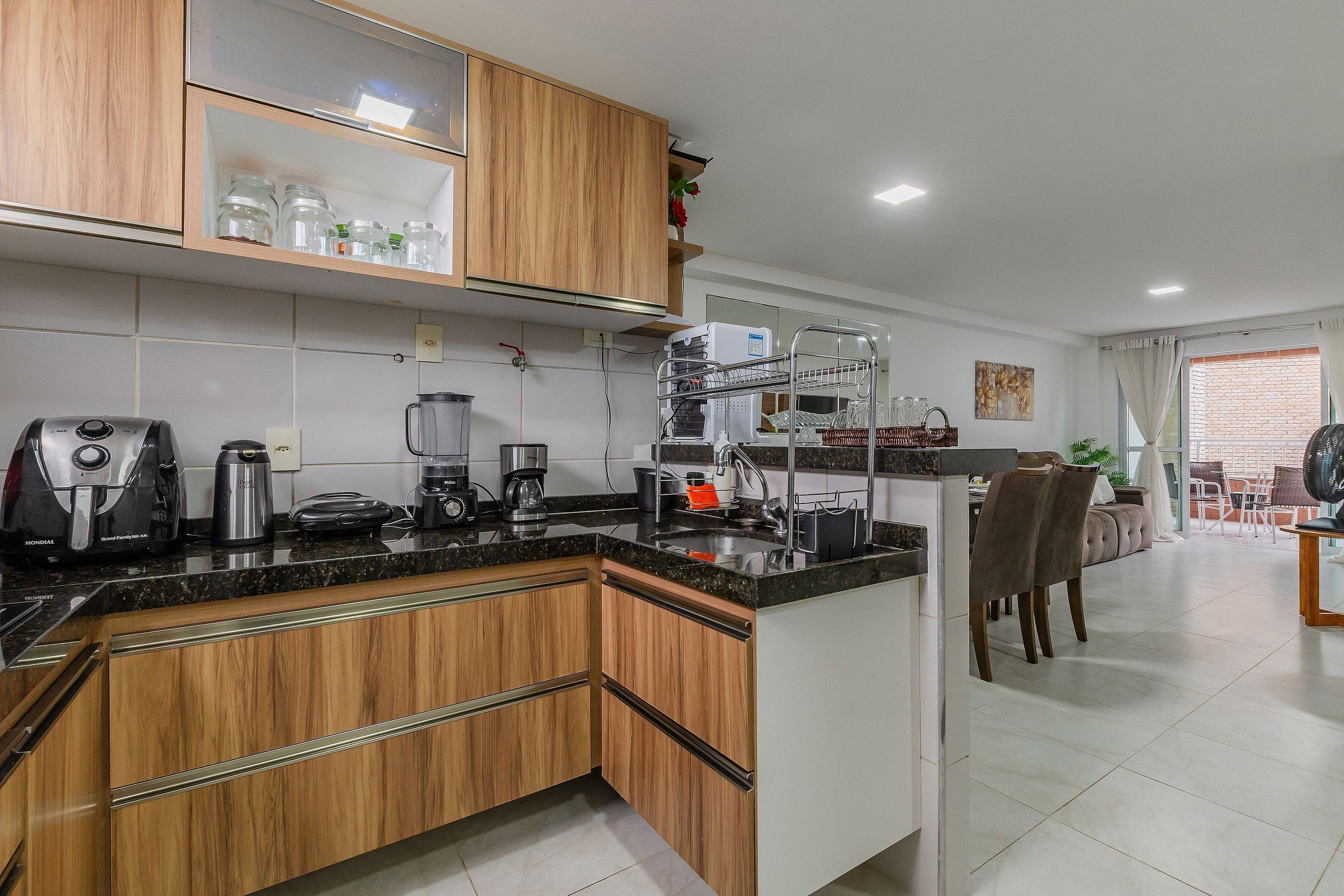 Una cocina moderna con armarios de madera, encimera negra y varios electrodomésticos, como una cafetera y una licuadora.