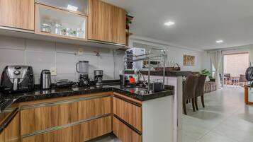 Una cocina moderna con armarios de madera, encimera negra y varios electrodomésticos, como una cafetera y una licuadora.