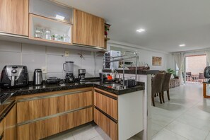 Una cocina moderna con armarios de madera, encimera negra y varios electrodomésticos, como una cafetera y una licuadora.