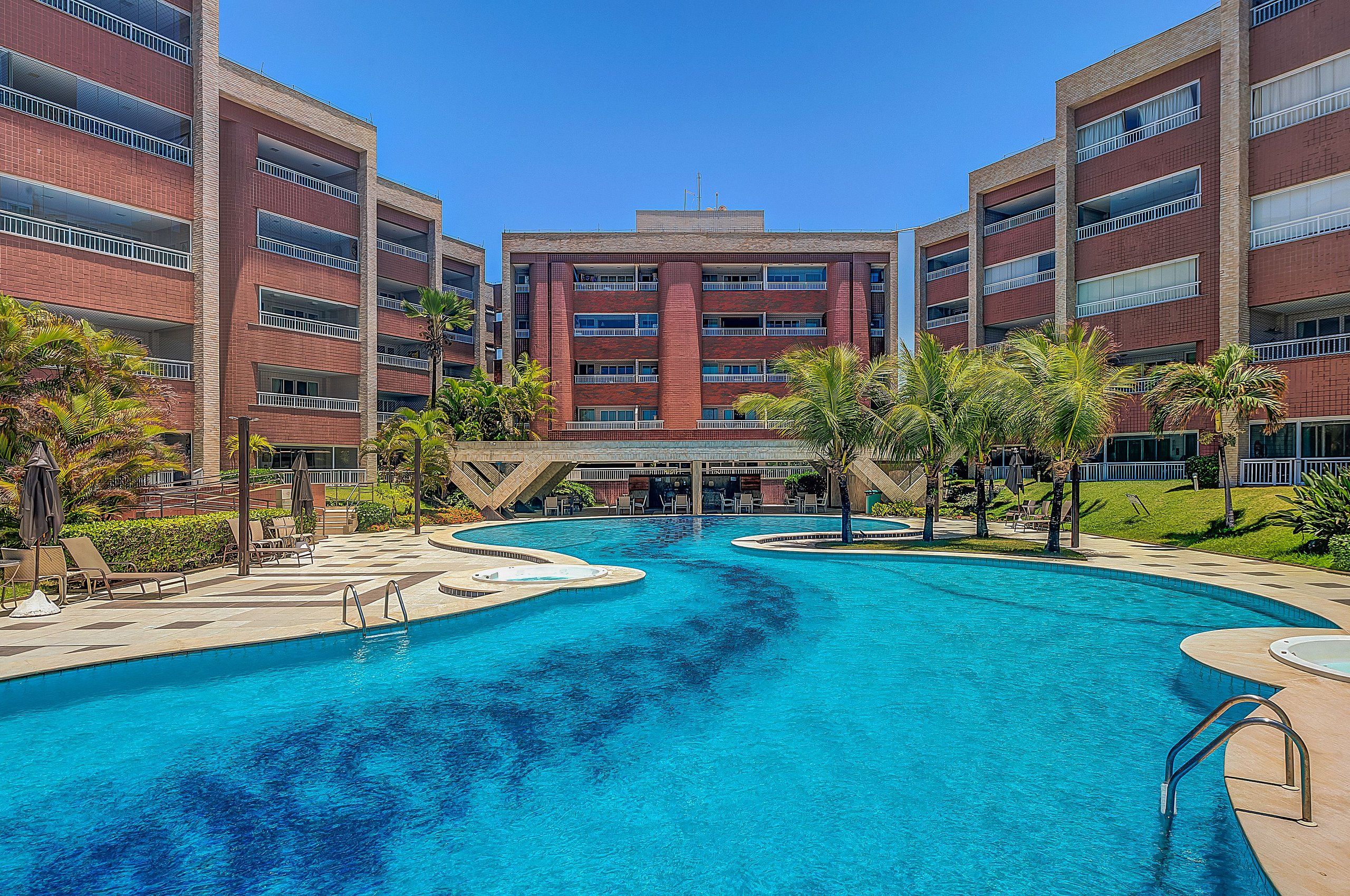 Un hotel con piscina central, varios balcones y un jardín ajardinado.
