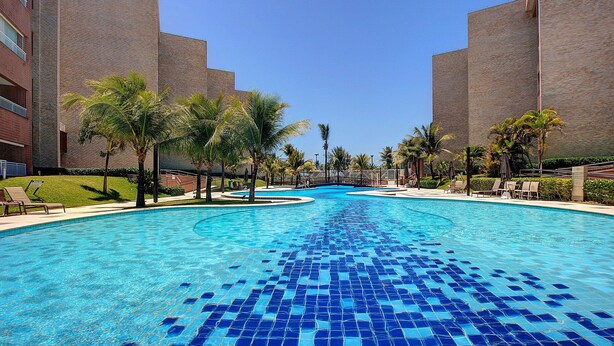 A swimming pool with blue mosaic tiles, surrounded by palm trees and a brick building. - Scopa Beach #c1-200 - Seafront by Carpediem (Aquiraz)