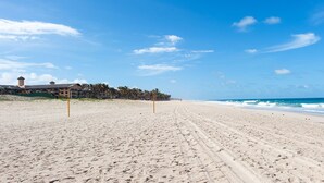 A wide sandy beach with footprints leading to the ocean, a building with a tower, and a clear blue sky. - Scopa Beach #c1-200 - Seafront by Carpediem (Aquiraz)