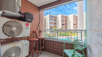A balcony with two chairs, a fan, and an air conditioner.
