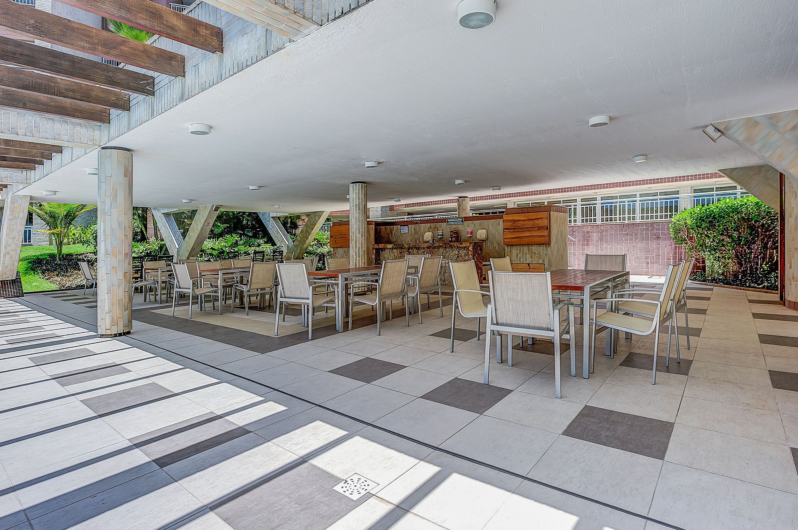An outdoor dining area with tables and chairs, a covered seating area, and a view of the building's interior.