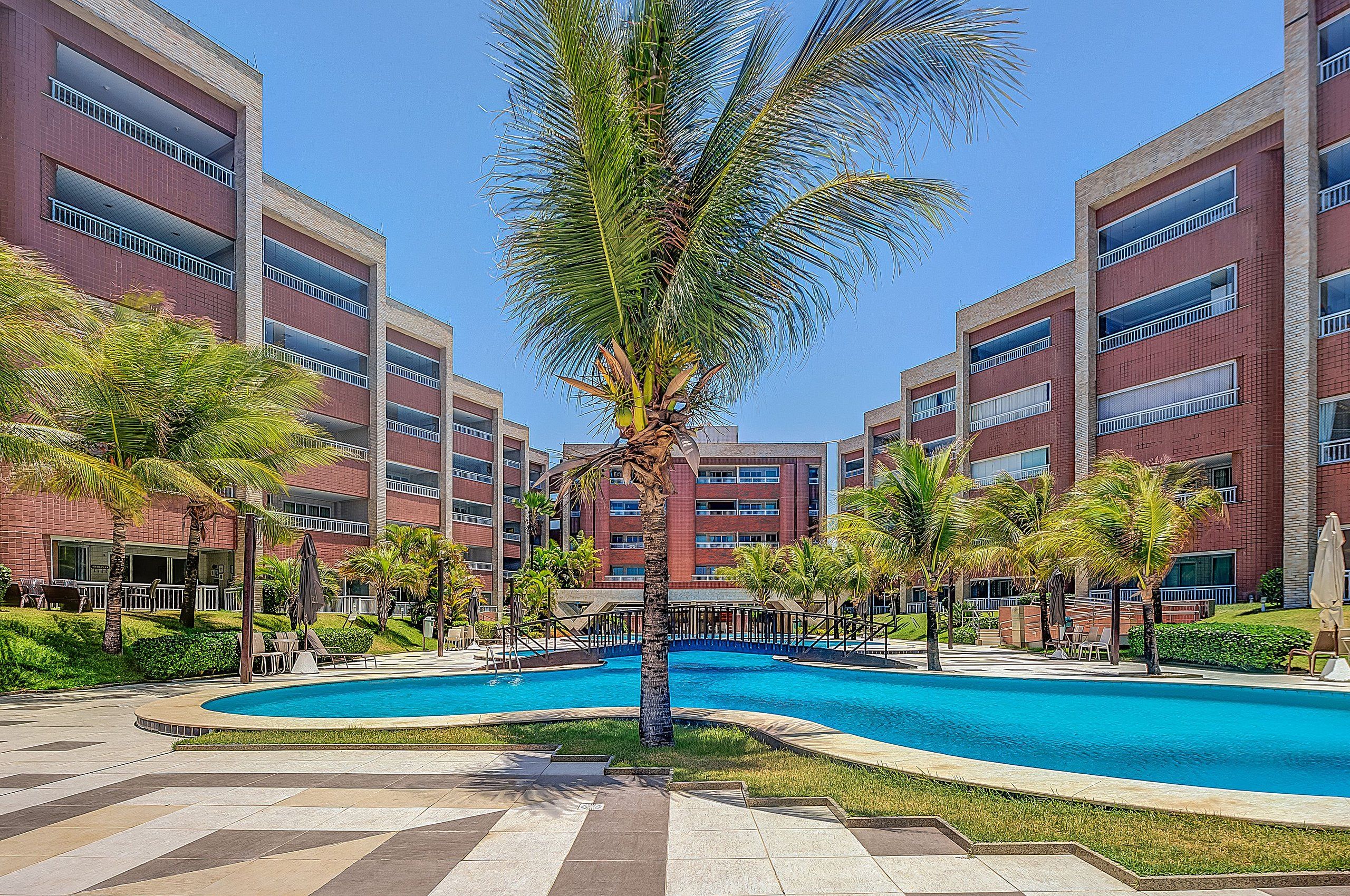 Un hotel con piscina, palmeras y fachada de ladrillo rojo.