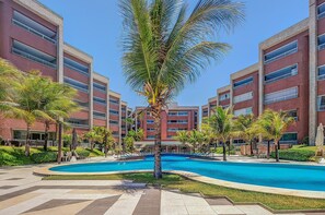 Ein Hotel mit Swimmingpool, Palmen und einer roten Backsteinfassade.