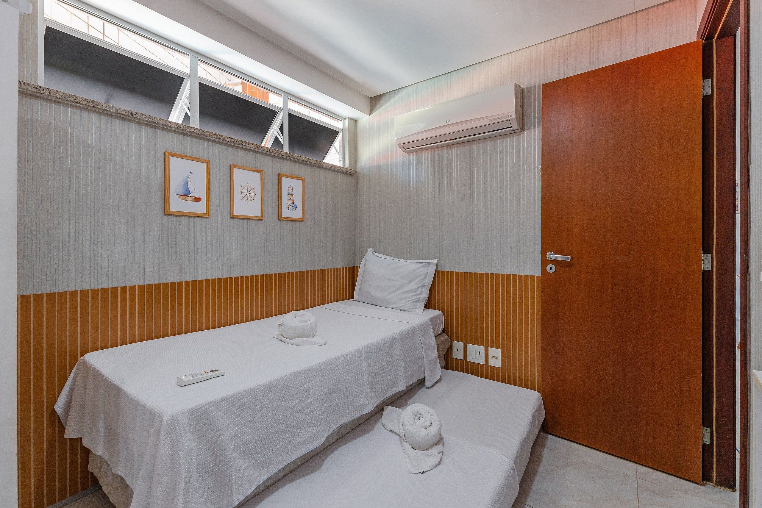 A hotel room with two beds, a window with a view, an air conditioning unit, and a door.