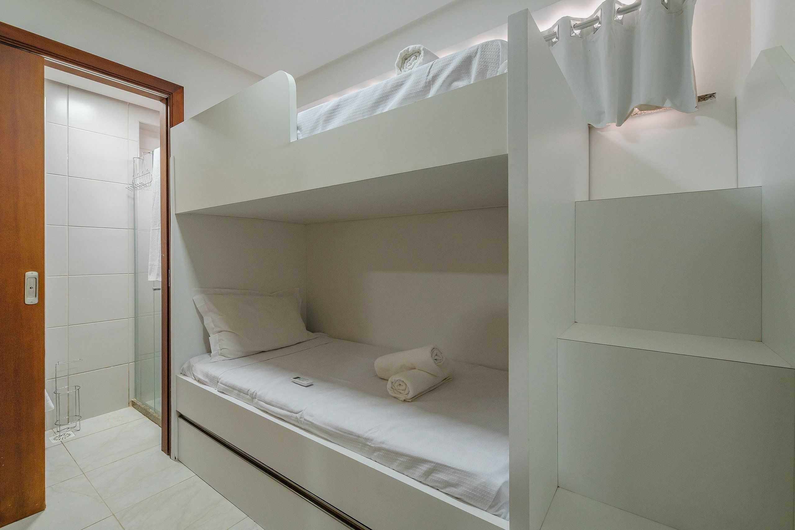 A bunk bed with a white mattress, a bedside table, and a wall-mounted light fixture.