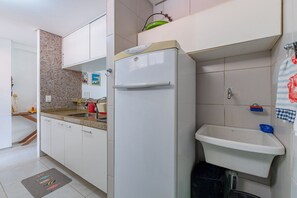 A kitchen with a white refrigerator, a sink, and a tiled backsplash. - Scopa Beach #c1-200 - Seafront by Carpediem (Aquiraz)