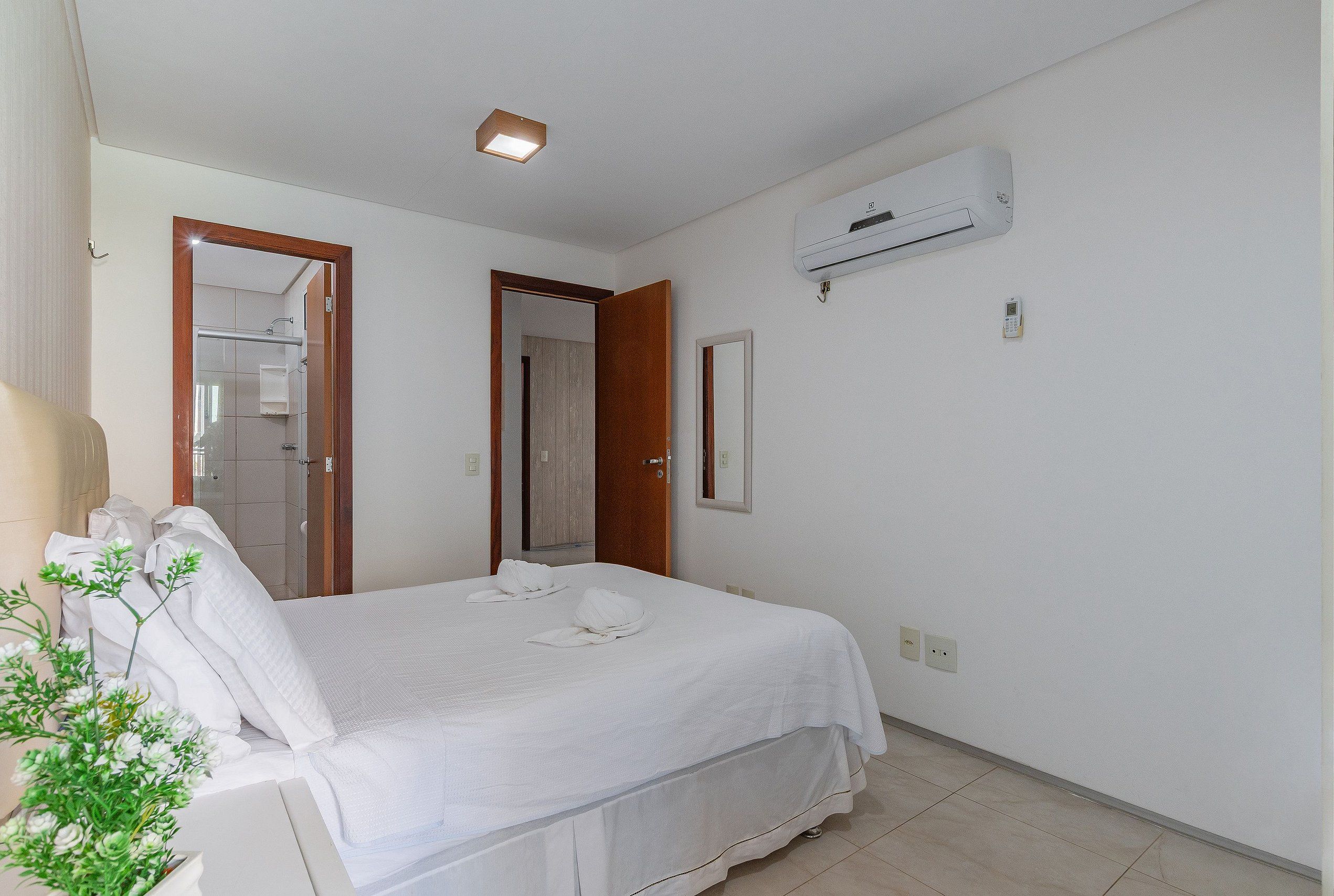 Habitación de hotel con cama, planta en maceta, equipo de aire acondicionado y puerta que da a un baño.