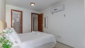 Habitación de hotel con cama, planta en maceta, equipo de aire acondicionado y puerta que da a un baño.