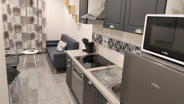 Eine kompakte Küche mit modernem Herd, einem Backofen und einem Kühlschrank. Es gibt eine kleine Essecke mit einem Tisch und einer Couch.