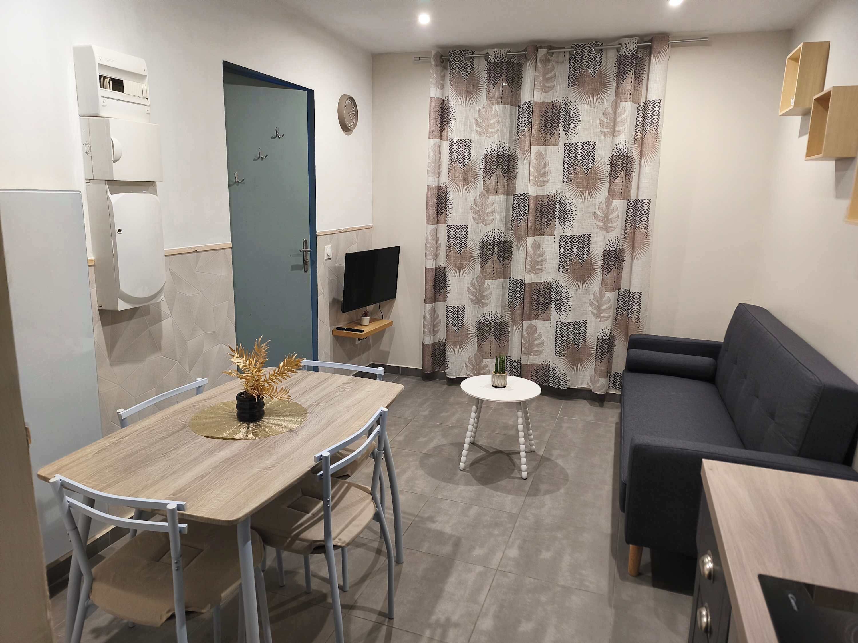Un espacio habitable compacto con una mesa de comedor, un sofá, un televisor y una cortina estampada.