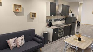 Ein kompakter Wohnbereich mit grauem Sofa, einem kleinen Esstisch und einer Küchenzeile.