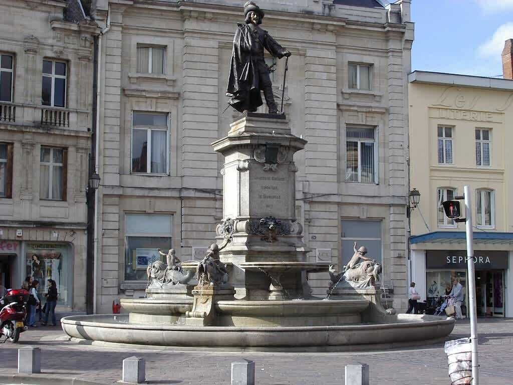 Ein öffentlicher Platz mit einem zentralen Denkmal, das eine Statue einer historischen Persönlichkeit zeigt.