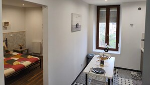 Ein modernes Zimmer mit einem Bett, einem Esstisch mit Stühlen, einer Uhr und einem Fenster mit Jalousien.