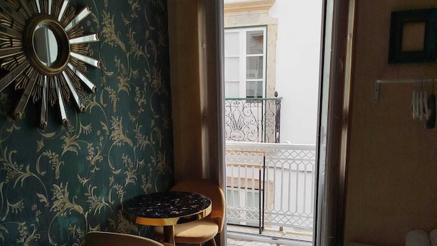 Una camera d'albergo con un letto, un tavolino rotondo con due sedie, uno specchio a parete e un balcone con ringhiera.