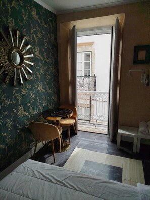 A hotel room with a bed, a small round table with two chairs, a mirror on the wall, and a balcony with a railing. - Modern Room in the Heart of Faro - Ideal for Couples and Travelers (Faro)