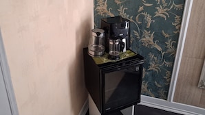 Un piccolo frigorifero nero con una macchina da caffè e una caraffa di vetro sopra, un quadro appeso alla parete e un interruttore della luce.