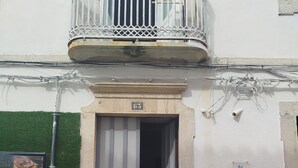 Un ingresso di un edificio con un balcone, una porta con il numero 63 e degli alloggiamenti per contatori a parete.