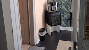 Un corridoio con una porta, un cestino, una macchina da caffè e un quadro appeso al muro.
