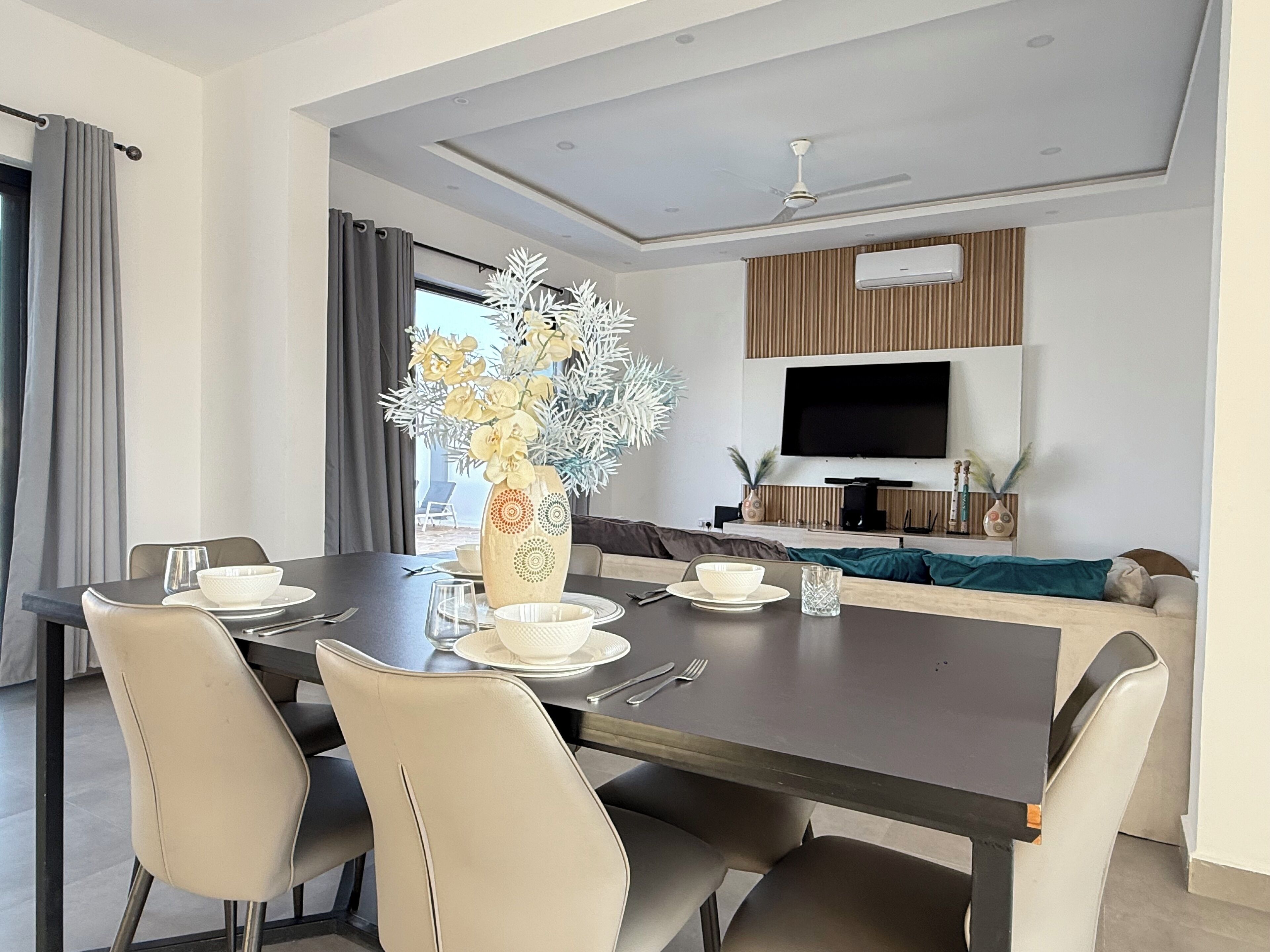 Un comedor moderno con una mesa de madera oscura, sillas color beige y un jarrón decorativo con flores.