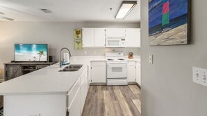 A modern kitchen with white cabinetry, a built-in microwave, and a large island with a sink. - Coastal Escape at Peachtree Place | 2BR Sleeps 8 | Near Beach & Attractions (Panama City Beach)