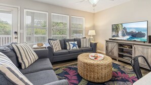 A living room with a gray sofa, a round woven ottoman, a flat-screen TV, and a wooden entertainment center. - Coastal Escape at Peachtree Place | 2BR Sleeps 8 | Near Beach & Attractions (Panama City Beach)
