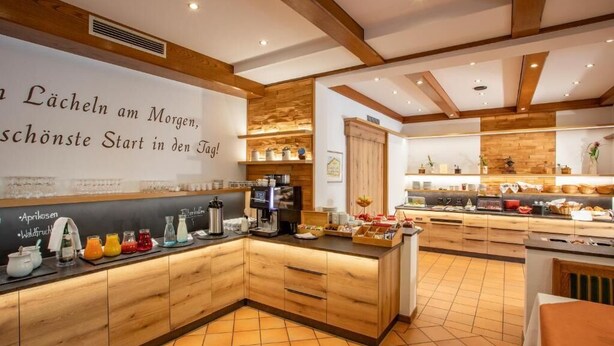 A modern kitchen with wooden cabinets, a coffee station, and a breakfast bar. - Gräfliches Hotel Alte Post (Bad Birnbach)