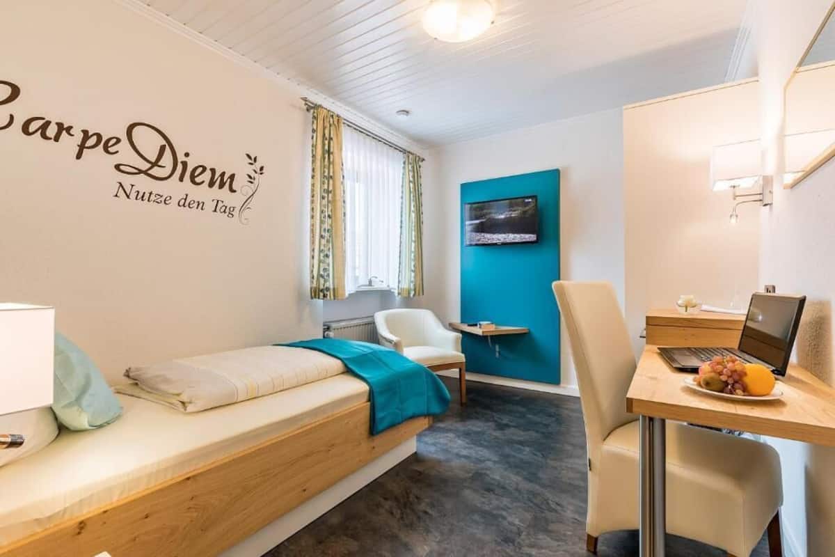 Una habitación con una cama, un escritorio con una computadora portátil, una silla, un televisor en la pared y un cartel en la pared.