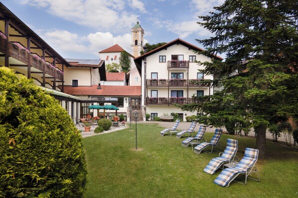 Un patio de hotel con césped, sillones de descanso, comedor y torre de campanas.