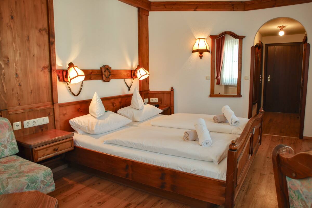 Un dormitorio con estructura de madera, dos camas, luces fijadas a la pared, un espejo y una puerta.