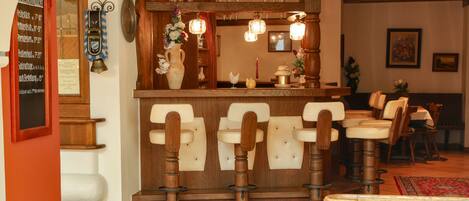 A restaurant interior with wooden bar stools, a counter with a vase of flowers, and a menu board on the wall.