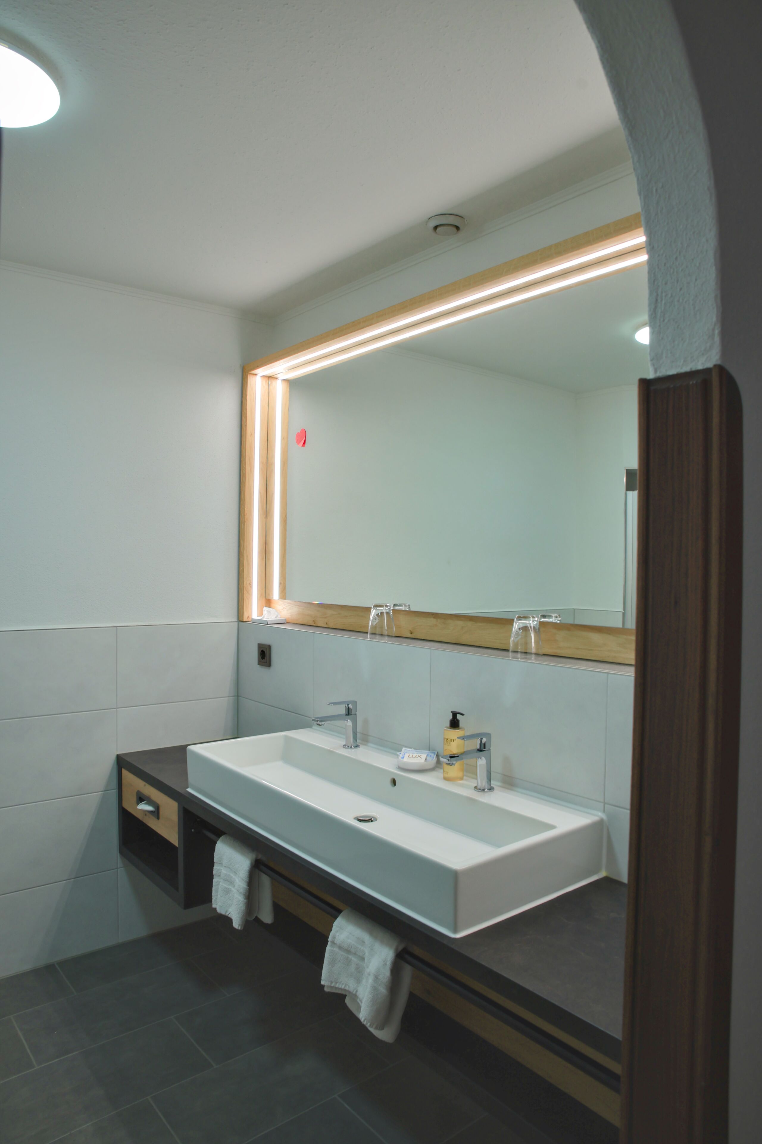 A modern bathroom with a large mirror, a white sink, and a towel rack.