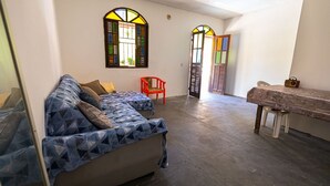 A room with a sofa, a table, and two chairs. There are two windows with stained glass. - Casa com Piscina em Coqueiro de Arembepe (Camaçari)