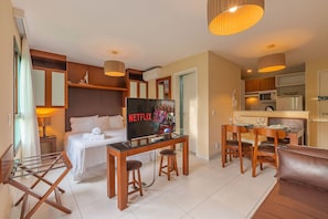 Una habitación de hotel con cama, televisor, escritorio, mesa de comedor y área de cocina.