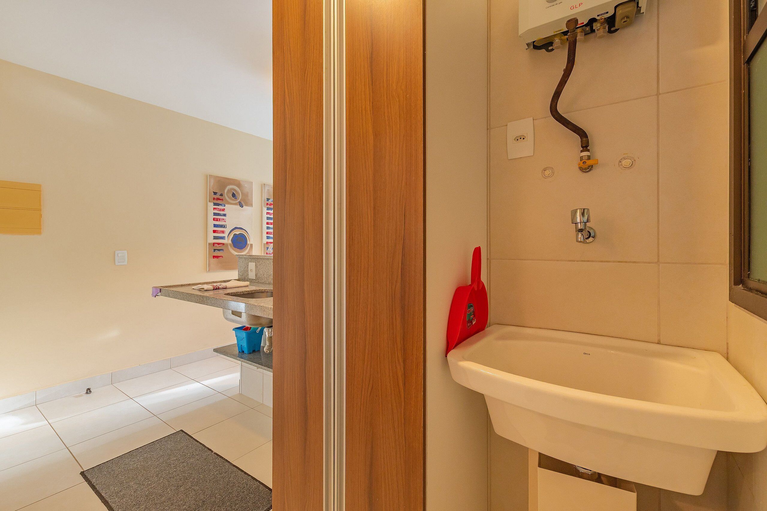 Un baño con un lavabo blanco, un cepillo rojo para limpieza y una zona de ducha con puerta de madera.
